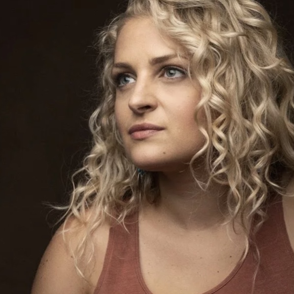 Eine junge Frau mit blonden, gelockten Haaren blickt verträumt. Mehr zu Ali Stroker