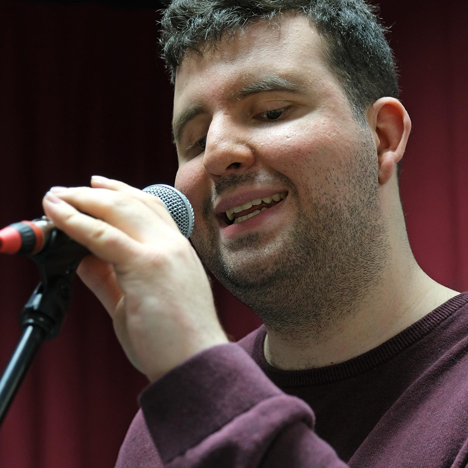 Porträt von Ersin Gülcan. Er singt und hat ein Mikrofon in der Hand. Er scheint sich in einem professionellen Setting zu befinden. 