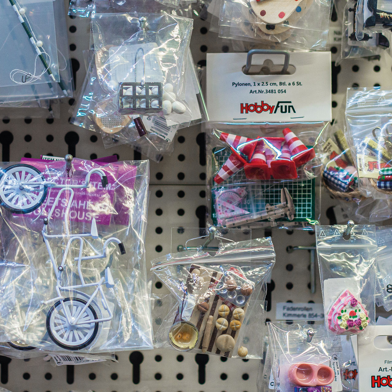 Allerlei kleine Spielzeuggegenstände wie ein Fahrrad oder ein Kuchen, hängen in Plastiktüten verpackt an einer Verkaufswand.