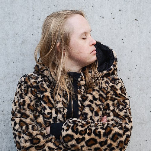 Portrait von Neele Buchholz. Eine junge Frau mit blonden Haaren, die einen Pullover mit Leopardenmuster trägt.