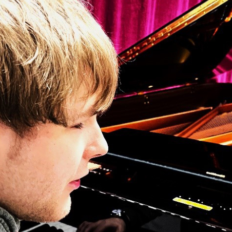 Das Foto ist schwarz-weiß. Er hat helle Haut und trägt eine dunkle Brille. Er lächelt mit geschlossenem Mund.