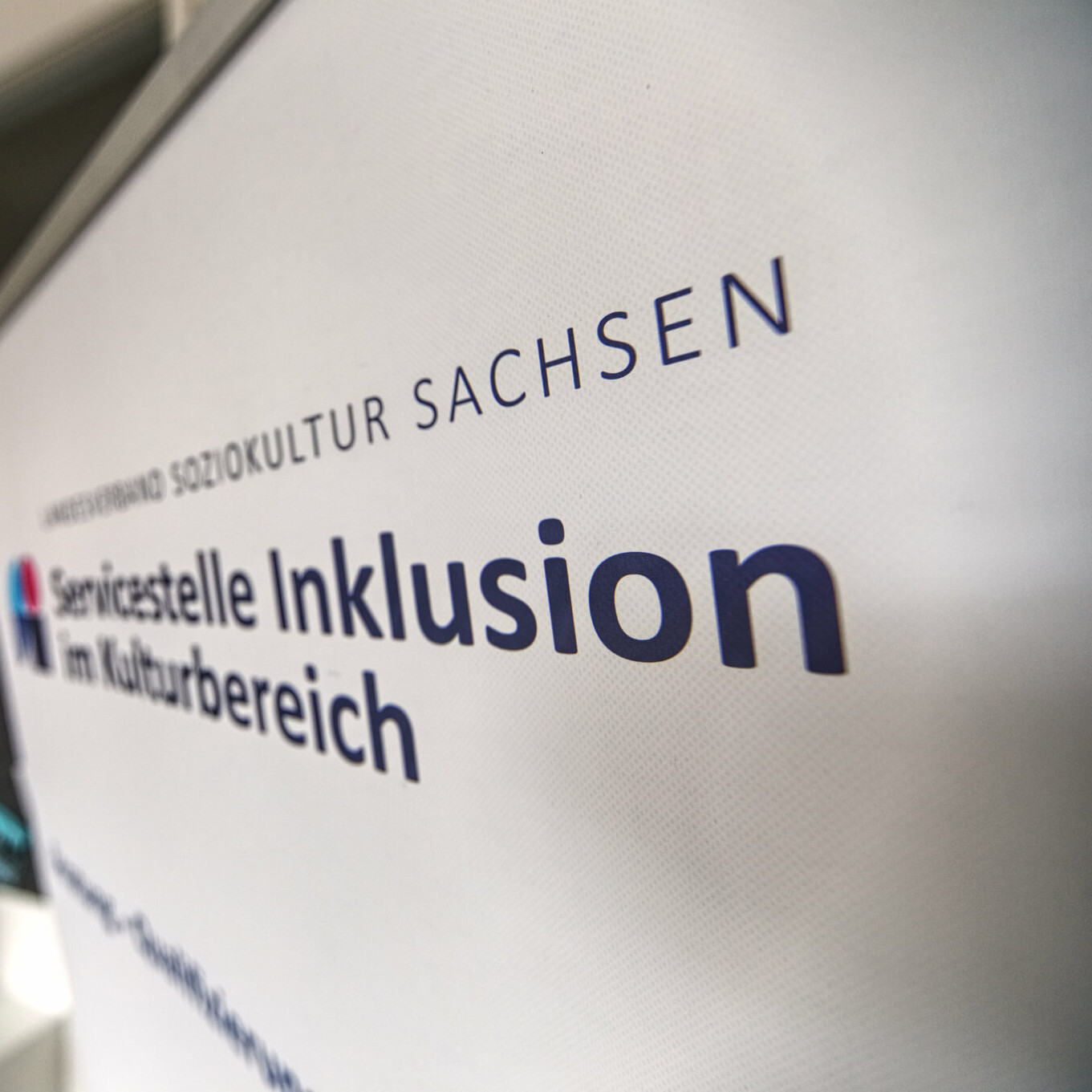 Ein weißes Schild mit der Aufschrift „Servicestelle Inklusion im Kulturbereich“ vom Landesverband Soziokultur Sachsen.