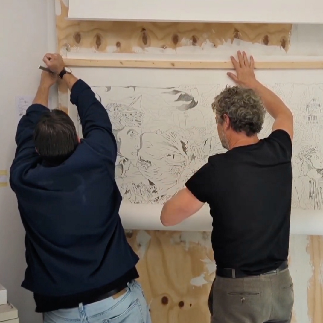 Zwei Personen hängen gemeinsam eine große Zeichnung an eine Wand.