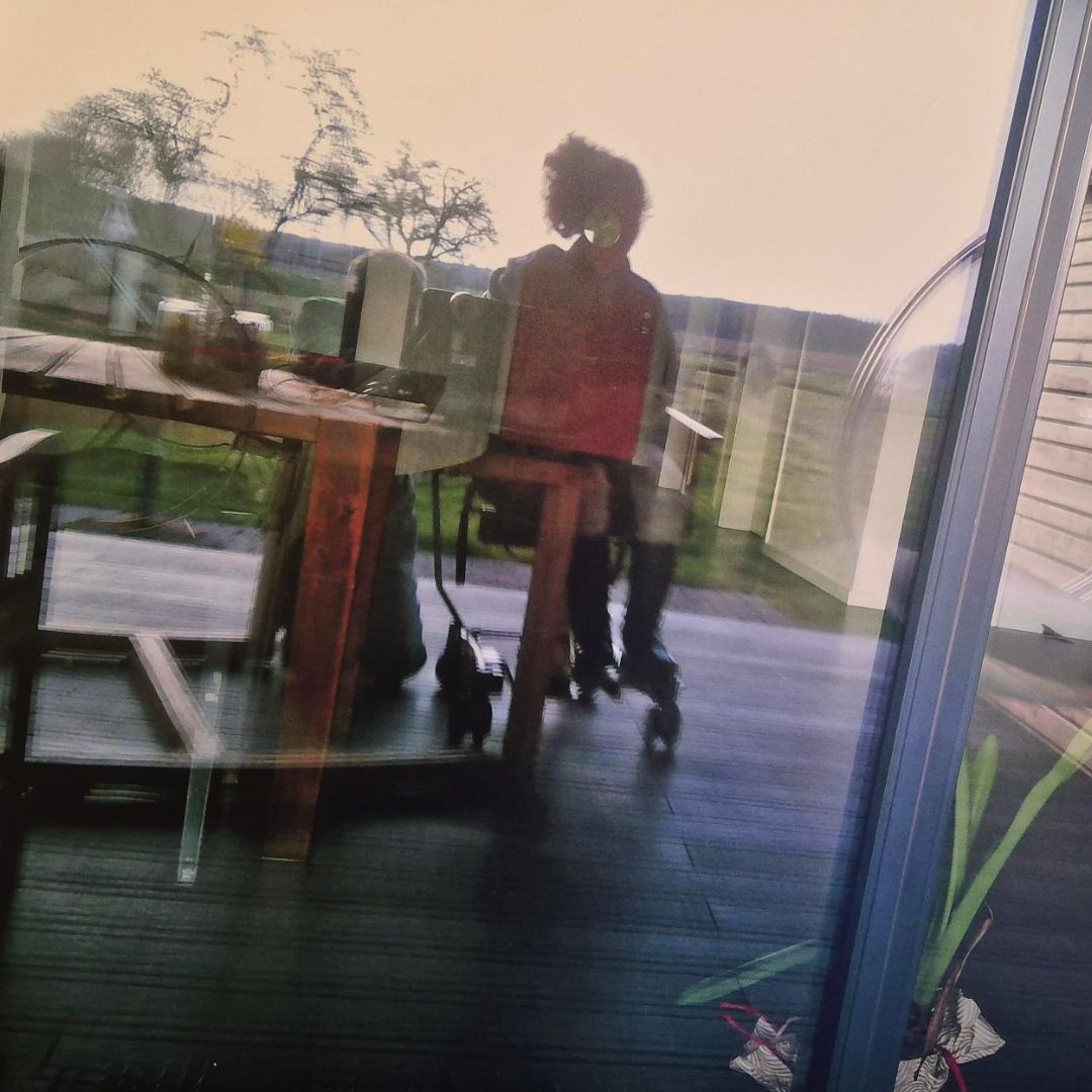 Ein verschwommener Blick auf eine Person, die an einem Tisch sitzt, reflektiert durch ein Fenster.