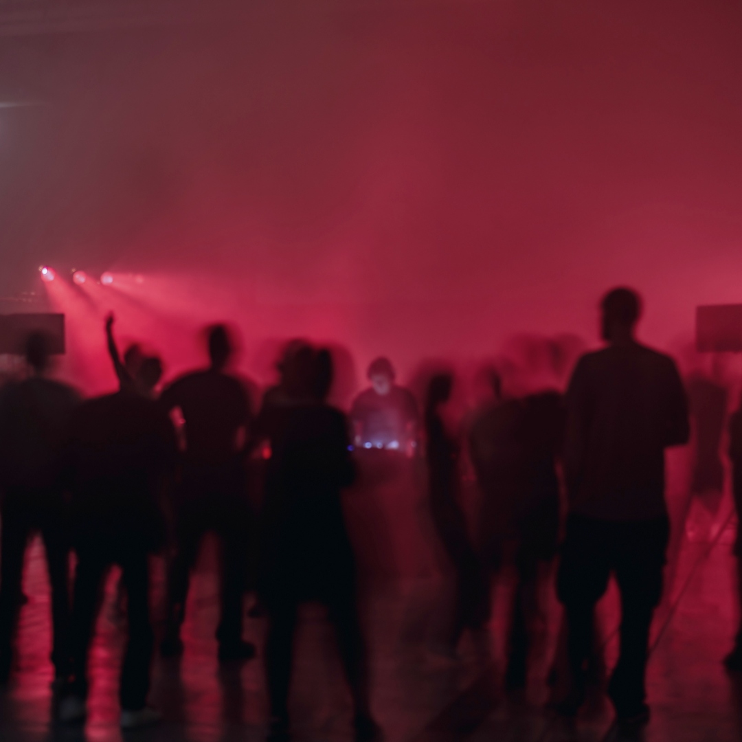 Menschen tanzen vor rotem Licht in einer nebligen Club-Atmosphäre.