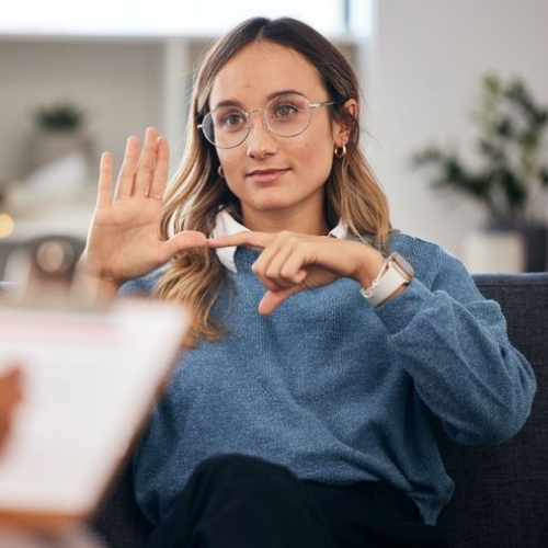 unge Frau mit Brille sitzt auf einem Sofa und kommuniziert mit Handgesten.