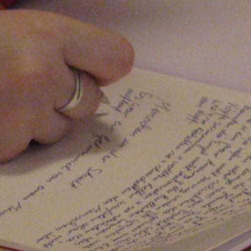 Hand schreibt Text auf ein Blatt Papier.
