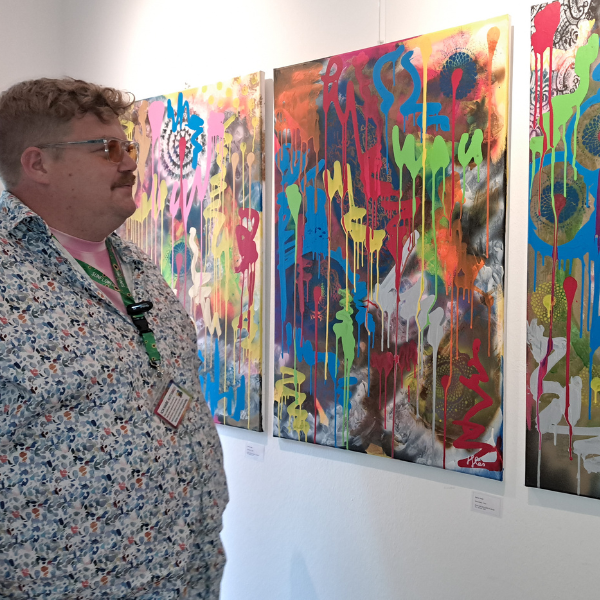 Dennis Henke betrachtet seine farbintensiven, abstrakten Gemälde in einer Ausstellung.