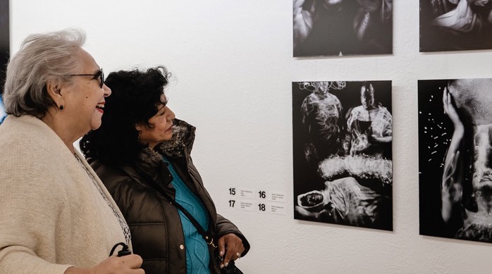 Zwei Museumsnesucherinnen betrachten Bilder, die von einem blinden Fotografen fotografiert wurden.